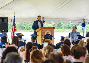 Man in a blue suit behind a podium giving a speech to graduates and guests